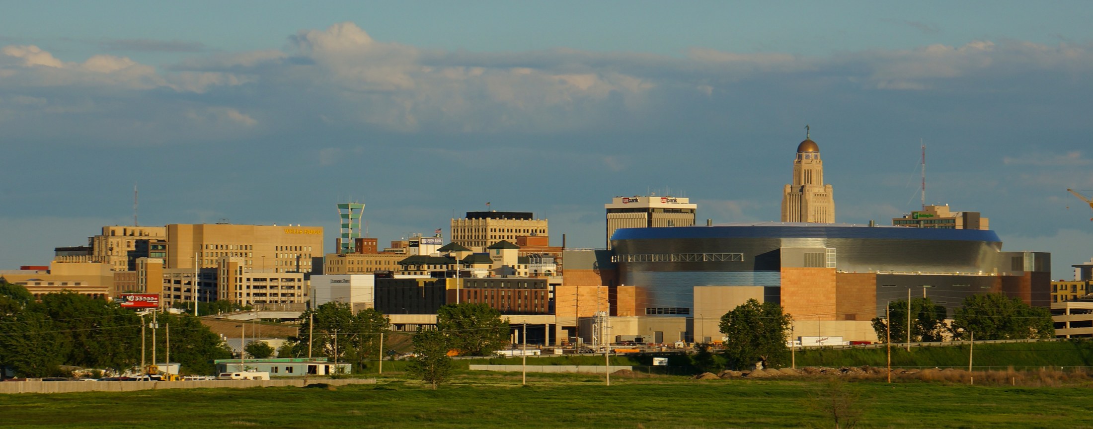 Lincoln, Nebraska skyline in warm evening light, with the State Capitol rising behind downtown buildings.