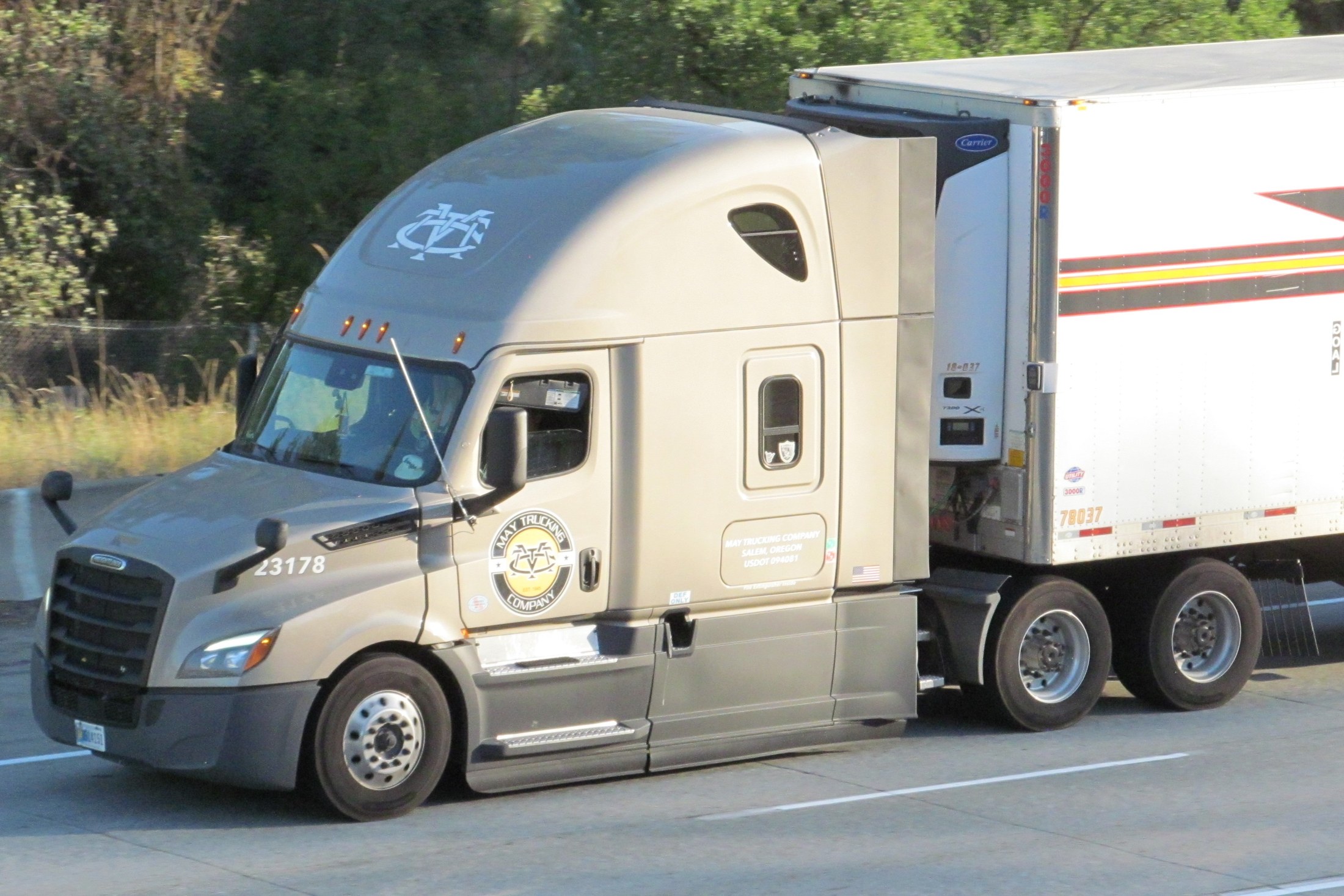 A silver American Freightliner tractor hauling an enclosed refrigerated box trailer on a highway.