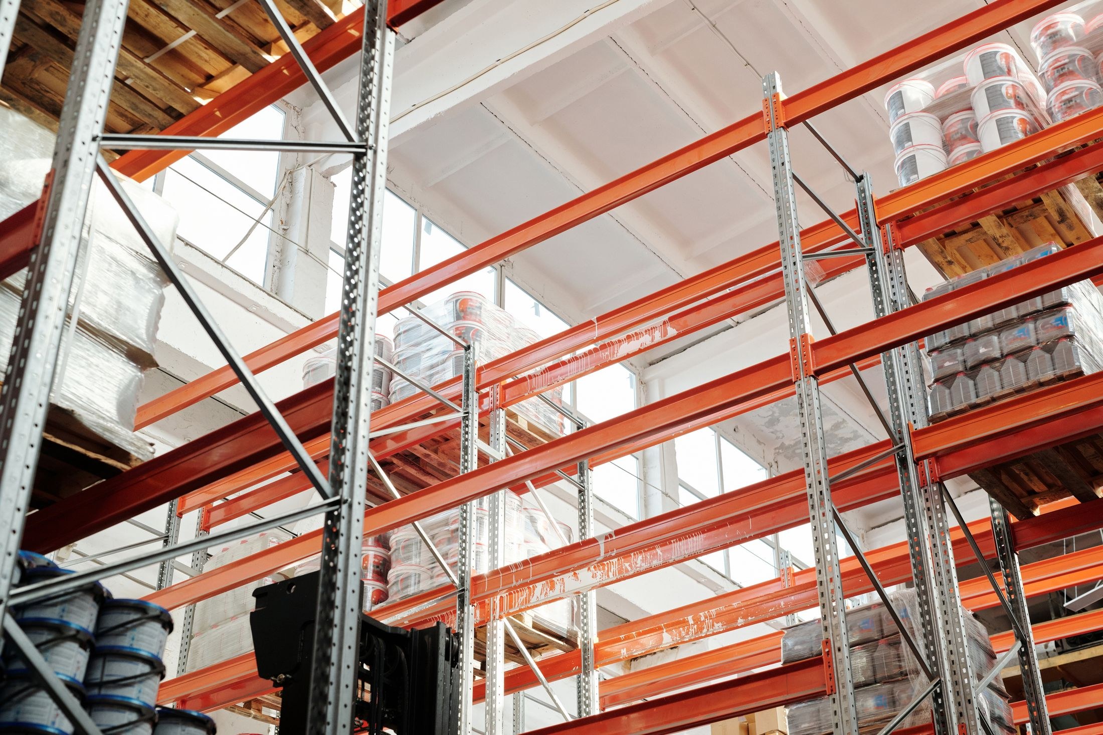 Bright industrial warehouse racks holding shrink-wrapped pallets of containers.