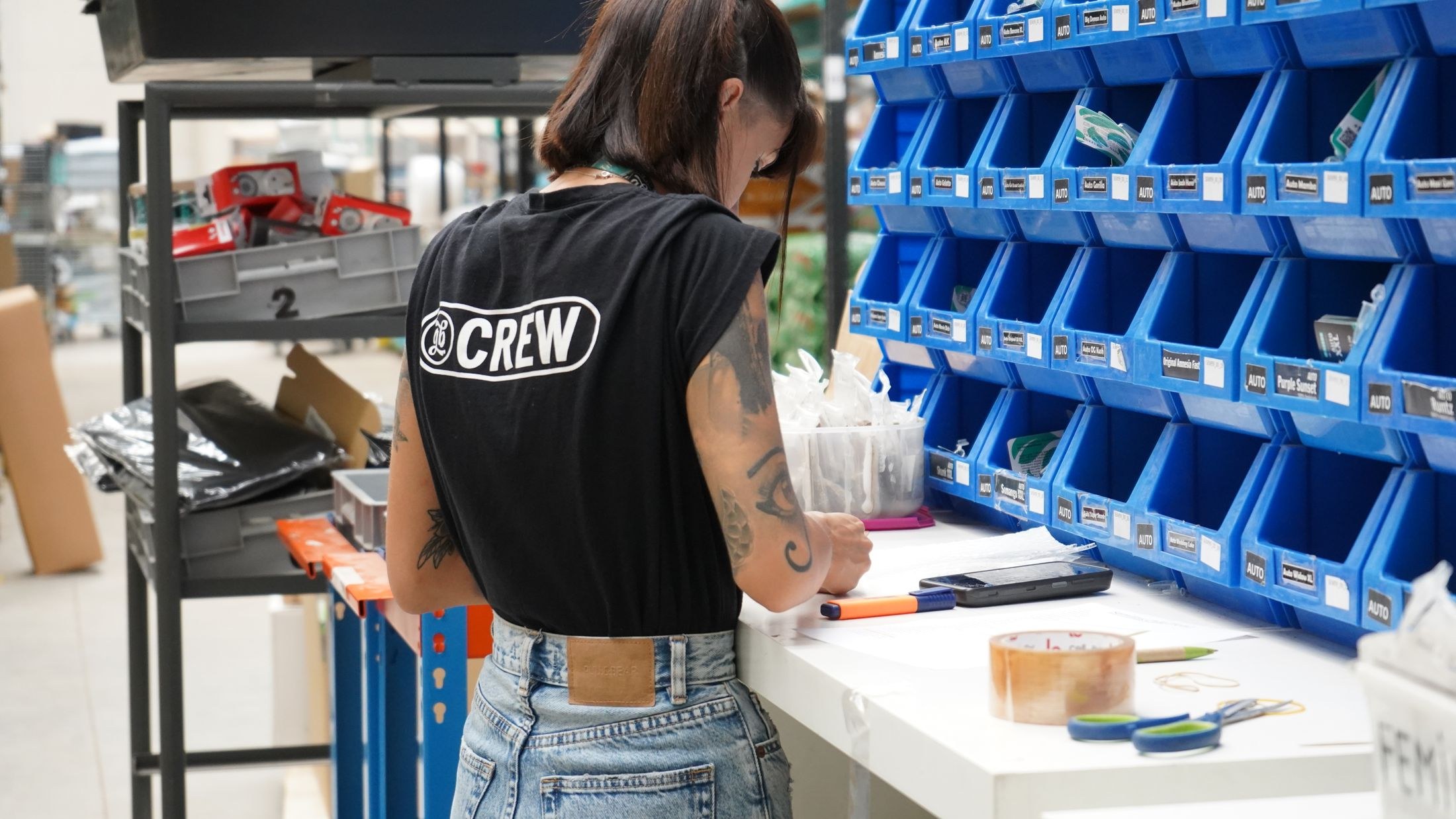 A warehouse worker checking small inventory items at a bench beside rows of blue storage bins.